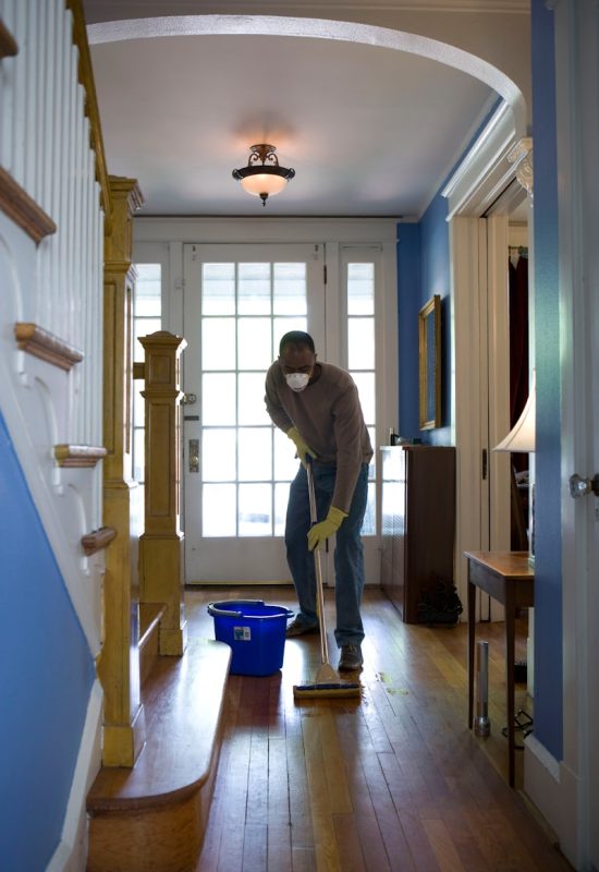 man in gray hoodie and blue denim jeans standing on brown wooden parquet flooring