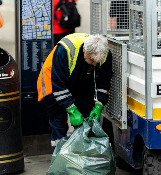 a man in a yellow safety vest and green gloves unloads a garbage bag